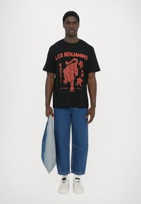 Black short-sleeve t-shirt featuring red graphic print with a tiger and text. Paired with wide-leg blue denim jeans and white sneakers.