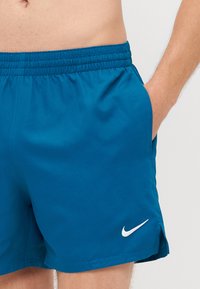 Kék Nike fürdőnadrág rugalmas derékkal, oldalzsebekkel és fehér swoosh logóval. Az anyagnak könnyű és sima a tapintása.
