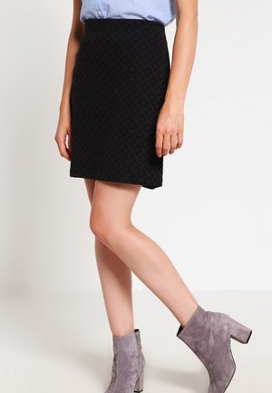 Kvinde iført sort tekstureret mininederdel, lyseblå skjorte stoppet ind og grå ruskindssko med blokhæle.