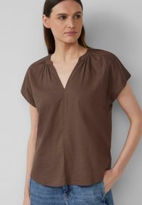 Blouse marron à manches courtes avec un décolleté en V et des détails froncés au niveau du cou. Fabriquée en tissu léger, elle présente une coupe décontractée.