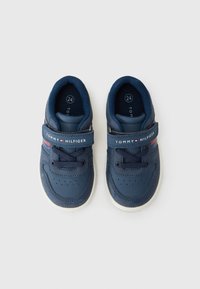 Blå lærersneakers med mesh-detaljer, rund tå, snøring og et borrelåsstropp med "TOMMY HILFIGER"-tekst i hvitt og rødt.