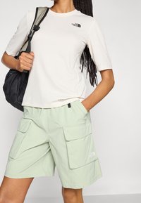 Lehké krémové tri čko s krátkým rukávem a texturovaným povrchem, doplněné o mátově zelené cargo šortky s velkými předními kapsami a logem.