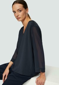 Marinebluse mit transparenten Dreiviertelärmeln, V-Ausschnitt-Design und gerafften Details an der Schulter. Weicher Stoff mit dezentem Fall.