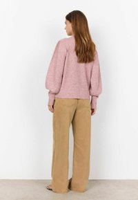 Helles rosa, geripptes Sweatshirt mit Ballonärmeln, kombiniert mit beigen, weit geschnittenen Hosen, die über Rückentaschen und dezente Steppdetails verfügen.