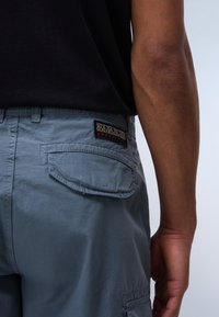 Pantalones cortos grises de carga con un bolsillo trasero y un parche de logo negro. Textura suave, corte recto, que cuenta con pasadores para cinturón y detalles de costura.