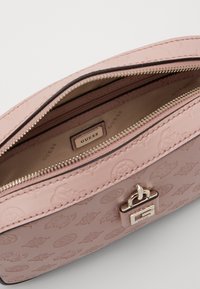 Rosa geprägte Handtasche mit Reißverschluss, die eine glatte Textur und ein auffälliges metallisches Logo-Detail auf der Vorderseite aufweist. Das Innere ist beige.