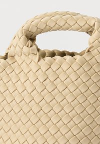 Μπεζ υφαντή τσάντα ώμου με υφή σε σχέδιο, διαθέτει στρογγυλεμένη κορυφαία λαβή και ευρύ άνοιγμα. Το υλικό φαίνεται μαλακό και ευλύγιστο.