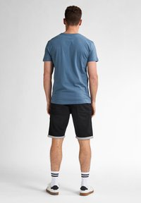 Helles blaues Baumwoll-T-Shirt für Herren mit Rundhalsausschnitt, kombiniert mit schwarzen Denim-Shorts mit umgeschlagenen Säumen. Weiße Sneaker mit schwarzen Akzenten.