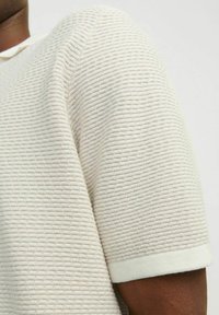 Texturovaný top s krátkým rukávem v světlé krémové barvě, se žebrovaným vzorem a zak cuffed rukávy, vyrobený z tkaniny s jemným povrchem.