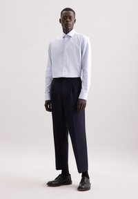 Camicia a quadratini blu chiaro abbinata a pantaloni navy scuri e scarpe nere. Taglio slim con un design strutturato e maniche lunghe.