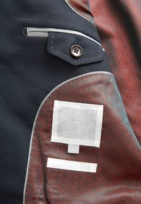 Tkanina marynarskiej kurtki z teksturową powierzchnią, z zapięciem na guzik, szarymi akcentami, wzorzystym wnętrzem oraz metkami do oznaczania.