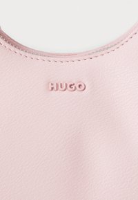 Pochette en cuir synthétique rose arborant le logo "HUGO" dans une couleur coordonnée, de forme arrondie et avec de fines coutures le long du zip.
