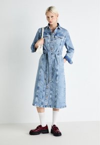 Ljusblå denimklänning med lång ärm, knappstängning, midjeband och två framfickor. Bärs med vita strumpor och bourgognefärgade platåskor.