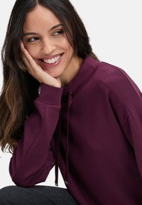 Bordowy sweter z wysokim kołnierzem i sznurkiem, z długimi rękawami i miękką fakturą, uzupełniony delikatnymi metalicznymi akcentami.