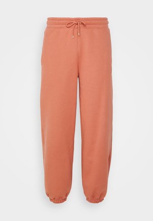 Persikka-väriset verkkarit, jotka on valmistettu pehmeästä kankaasta. Niissä on joustava vyötärö, jossa on nyöri, sivutaskut ja elastiset hihnat nilkoissa.