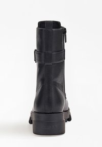 Bottine noire en simili cuir avec une finition texturée, fermeture éclair sur le côté et deux sangles autour de la tige. Semelle en caoutchouc plate avec un logo sur le talon.