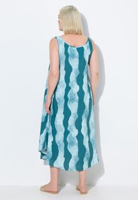 Ein ärmelloses aquafarbenes Kleid mit einem wellenförmigen weißen Muster, das einen runden Rücken und eine lockere Passform hat und knapp über den Knöcheln endet.