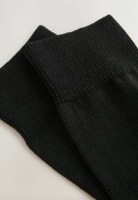 Melnas adītas zeķes ar ribotu tekstūru un gludu augšējo malu, kārtīgi salocītas ar plakanu malu, radot elegantu un kompaktu izskatu.