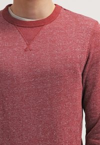 Czerwony sweter z teksturą, z prążkowanym, okrągłym dekoltem. Charakteryzuje się nakrapianym wzorem i wzmocnionym szwem na ramionach.