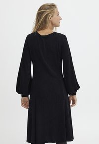 Svart klänning med långa puffärmar, U-formad halsringning och ett flödande silhuett. Tillverkad av textil med subtil lyster.