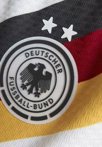 Écusson de l'équipe nationale d'Allemagne sur un tissu avec des rayures noires, rouges et jaunes. Présente un emblème d'aigle, deux étoiles blanches et "Deutscher Fussball-Bund."