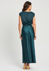 Turkizna satenska maksi obleka s kratkimi rokavi, elastičnim pasom in gladko teksturo. Oblikovanje vključuje sproščen kroj in sega do tal.