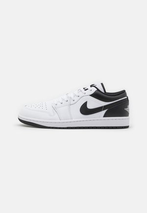 Baskets basses Nike blanches et noires avec bout perforé, logo swoosh noir et col rembourré sur fond blanc.