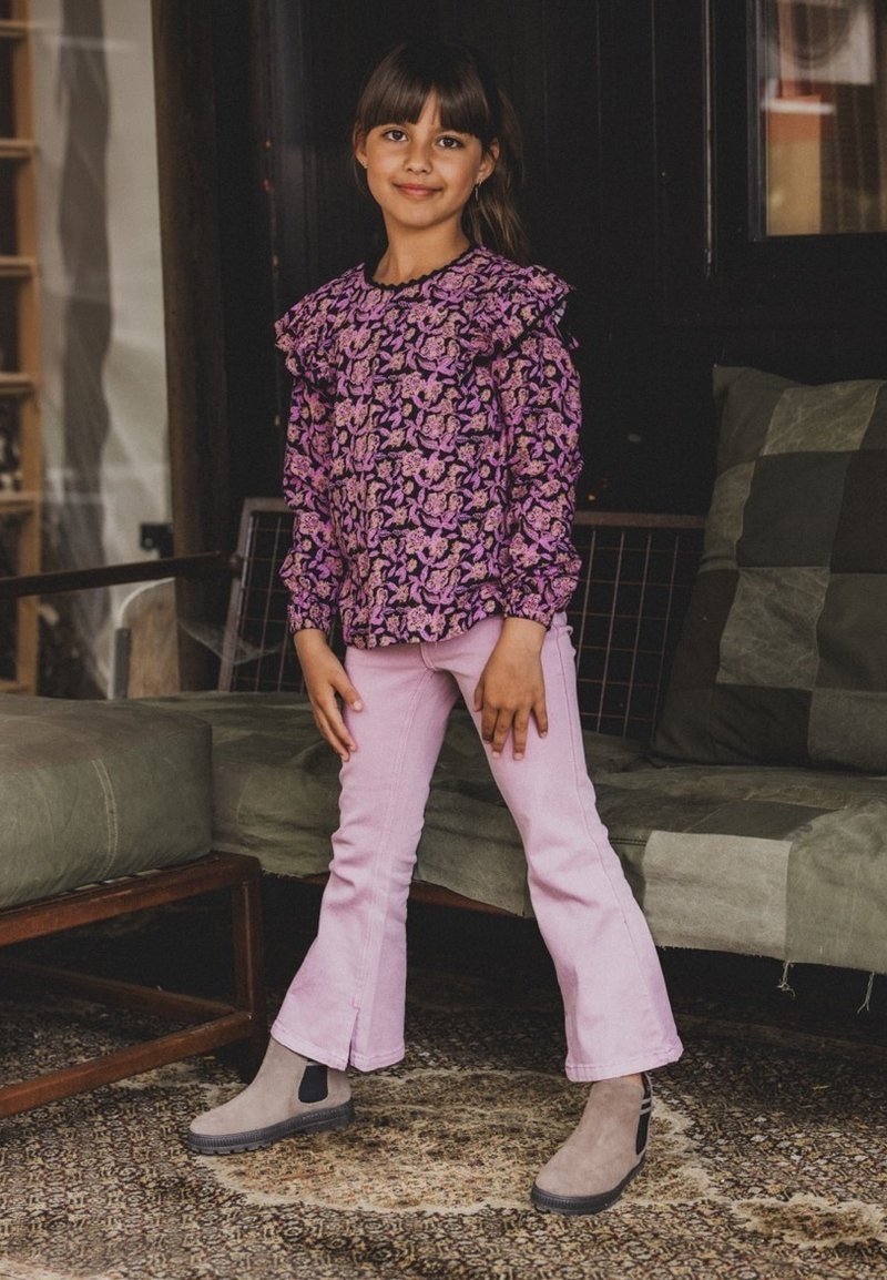 Paarse bloemen blouse met lange mouwen en rimpelrand bij de hals, gecombineerd met lichtroze flared broeken en grijze enkellaarsjes met zwarte accenten.