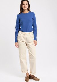 Langsleeve blauwe top, crèmekleurige broek en bruine leoprint schoenen. Broek is opgerold bij de boorden. Subtiele textuur in de stof.