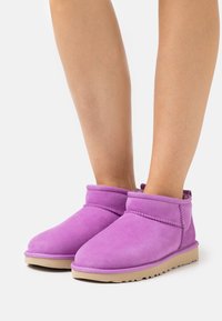 Bottines en daim violet avec un bout arrondi, une texture douce, et une semelle plate beige. Elles présentent des coutures contrastantes et un revers plié.