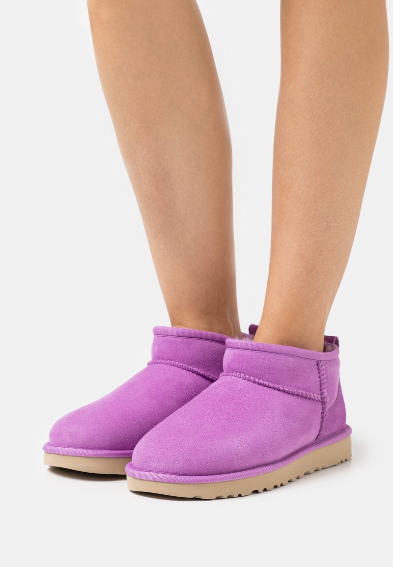 Bottines en daim violet avec un bout arrondi, une texture douce, et une semelle plate beige. Elles présentent des coutures contrastantes et un revers plié.