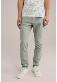 Pantaloni din bumbac de culoare verde deschis, cu croială slim, asociați cu un tricou alb cu dungi. Purtați cu teneși bej, care pun în evidență un material texturat.