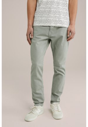 Pantaloni din bumbac de culoare verde deschis, cu croială slim, asociați cu un tricou alb cu dungi. Purtați cu teneși bej, care pun în evidență un material texturat.