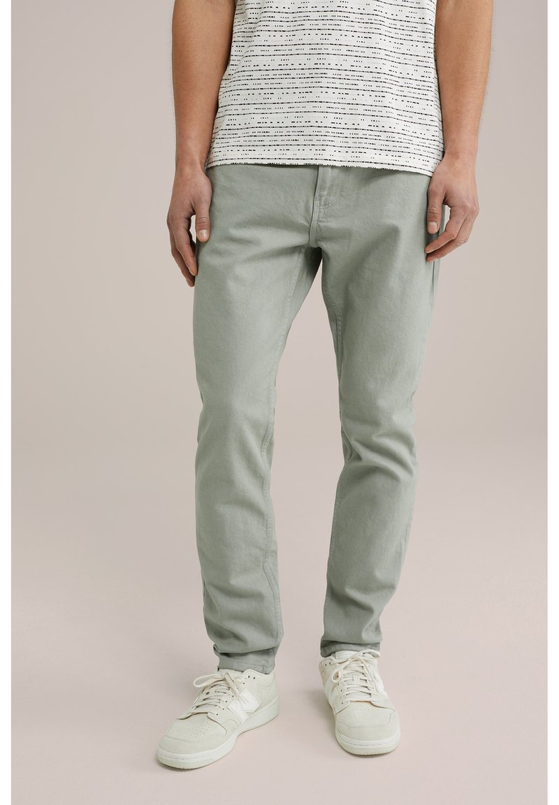 Pantaloni din bumbac de culoare verde deschis, cu croială slim, asociați cu un tricou alb cu dungi. Purtați cu teneși bej, care pun în evidență un material texturat.