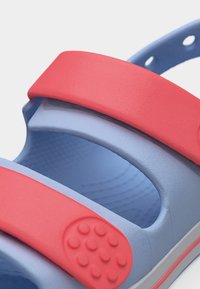 Κοντινό πλάνο ενός παιδικού σανδαλιού μπλε και κόκκινο με ρυθμιζόμενους ιμάντες και υφή στη σόλα για ασφαλή εφαρμογή και άνεση.
