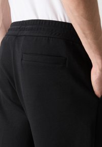 Čierne jogger nohavice s elastickým pásom, jednou zadnou vreckom a mäkkým bavlneným materiálom, prezentované v priliehavom strihu.