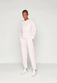Jasnoróżowa bluza z kapturem i pasujące joggery wykonane z miękkiego materiału, z przednią kieszenią, kapturem ze sznurkiem i elastycznymi mankietami. W zestawie z białymi sneakerami.