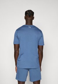 Camiseta atlética azul hecha de tejido transpirable, con mangas cortas, cuello redondo y un pequeño logotipo blanco en la parte posterior.