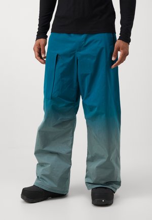 Blauw en teal gradient sneeuwbroeken gemaakt van lichtgewicht materiaal, met een zijzak en een relaxed fit, gecombineerd met zwarte sneeuwboots.