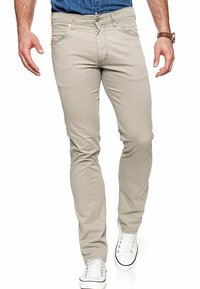 Beige katoenen broek met een slim fit, voorzien van een rits en zijzakken. Draagt een blauwe shirt met witte sneakers. Soepele textuur.