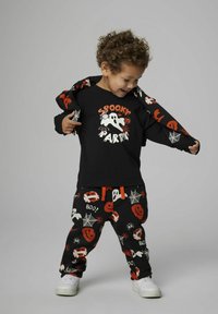 Zwarte langekleurige shirt met een spookontwerp en de tekst "Spooky Party", gecombineerd met zwarte broek met Halloween-patronen van spoken, pompoenen en spinnen.