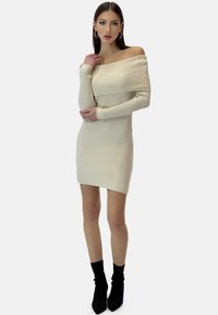 Vestido de punto acanalado color crema, con escote hombros descubiertos, mangas largas, silueta ajustada y dobladillo recto. Combina con botines negros.