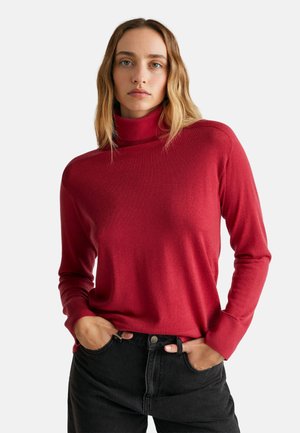 Roter Rollkragenpullover aus weichem Strickmaterial, mit langen Ärmeln und einem lässigen Schnitt, kombiniert mit hochgeschnittenen schwarzen Jeans.