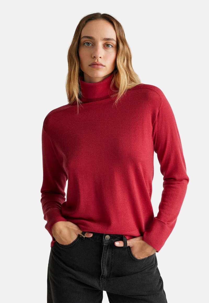 Roter Rollkragenpullover aus weichem Strickmaterial, mit langen Ärmeln und einem lässigen Schnitt, kombiniert mit hochgeschnittenen schwarzen Jeans.