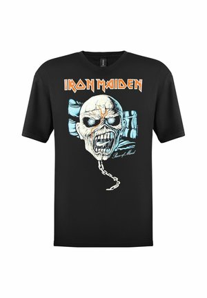 Svart bomull T-skjorte med et grafisk trykk av et hodeskalle og kjede foran, med teksten "IRON MAIDEN" over i oransje. Korte ermer, rund hals.