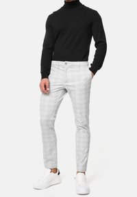 Hellgraue gemusterte Hosen im Slim-Fit-Schnitt, kombiniert mit einem schwarzen Rollkragenpullover und weißen Sneakers. Mit Fronttaschen und einem Knopfverschluss ausgestattet.