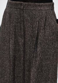 Jupe taille haute gris foncé avec un motif en chevrons portée sur un top noir, montrant des plis avant et une partie de la ceinture.