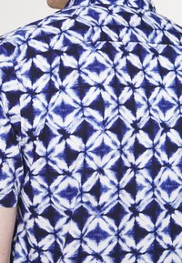 Korte mouwen shirt met een marineblauw en wit geometrisch patroon met diamantenvormen en een zachte stoftextuur. Ontwerp met knoopsluiting op de kraag.