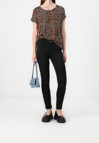 Haut à manches courtes en imprimé léopard, jean skinny noir avec des accents côtelés, et chaussures noires épaisses. Un sac à main bleu clair complète le look.