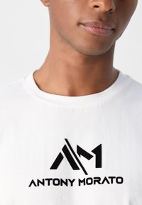 T-shirt en coton blanc avec un logo noir proéminent portant le texte "ANTONY MORATO". Col rond, texture lisse et manches courtes.